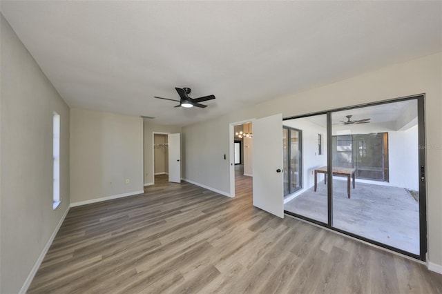 spare room featuring baseboards, plenty of natural light, light wood finished floors, and ceiling fan with notable chandelier