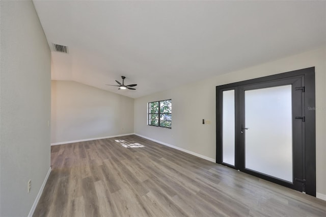 spare room featuring lofted ceiling, visible vents, a ceiling fan, wood finished floors, and baseboards