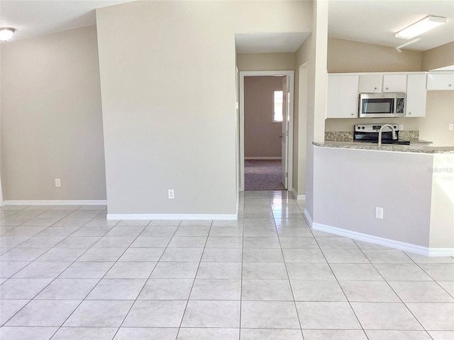 kitchen with light tile patterned floors, baseboards, lofted ceiling, appliances with stainless steel finishes, and white cabinetry