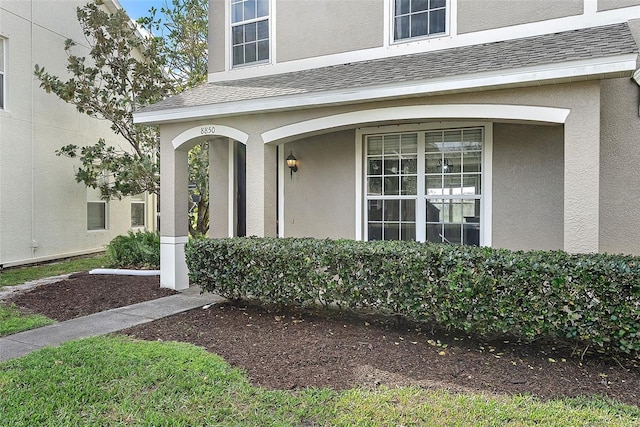 entrance to property featuring a shingled roof and stucco siding