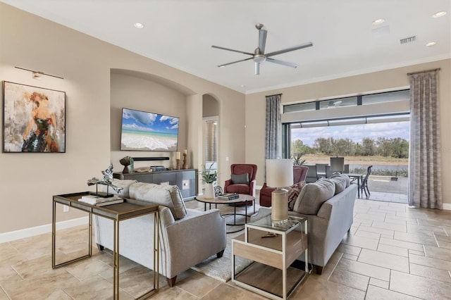 living room featuring arched walkways, ornamental molding, stone tile floors, and baseboards