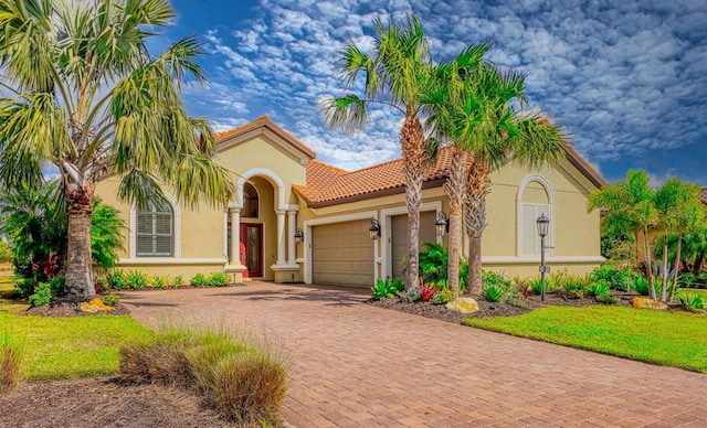 mediterranean / spanish-style home with decorative driveway, a tile roof, an attached garage, and stucco siding