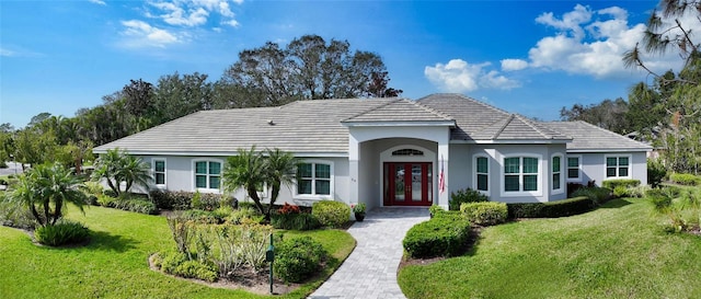 ranch-style house with stucco siding, a tiled roof, a front yard, and french doors