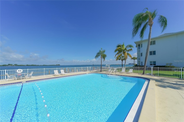 community pool with a water view, fence, and a patio