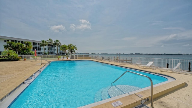 pool with a water view, fence, and a patio area