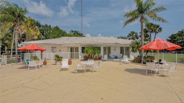 rear view of house with a tile roof, fence, outdoor dining space, and a patio area