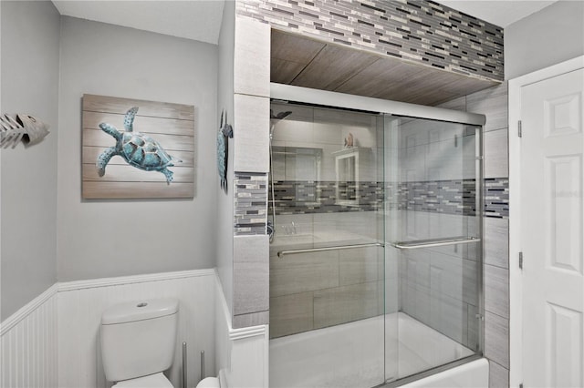 full bathroom with a wainscoted wall, combined bath / shower with glass door, and toilet