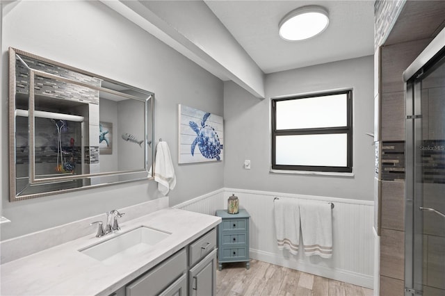 full bath featuring wainscoting, tiled shower, vanity, and wood finished floors