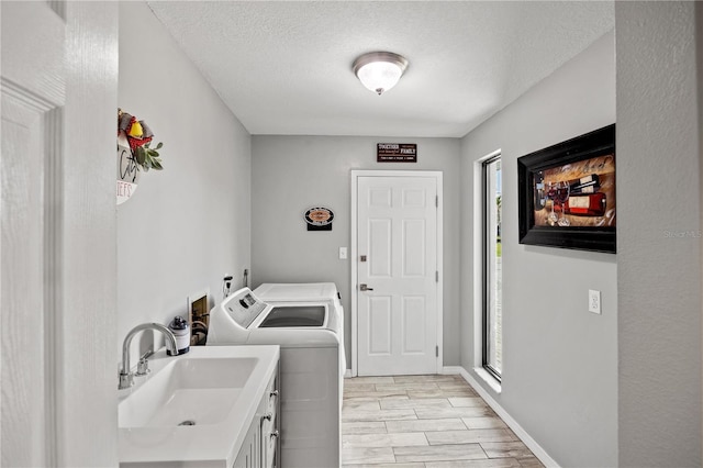 washroom featuring washing machine and clothes dryer, cabinet space, a sink, a textured ceiling, and baseboards