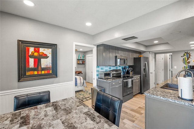 kitchen featuring visible vents, appliances with stainless steel finishes, gray cabinetry, stone counters, and a sink