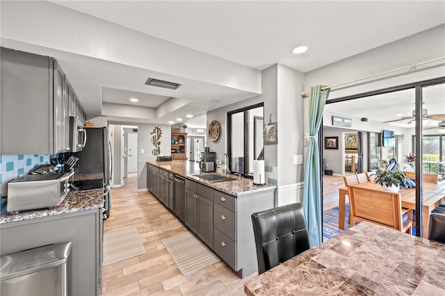 kitchen featuring stainless steel appliances, a sink, open floor plan, light wood-type flooring, and light stone countertops