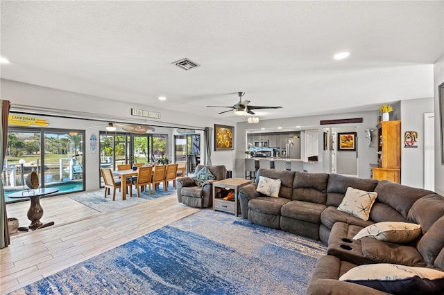 living area with light wood-style flooring, visible vents, ceiling fan, and a textured ceiling