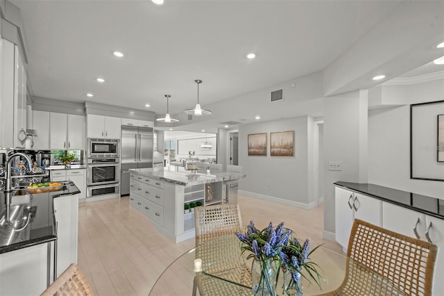 kitchen with built in appliances, a kitchen island, visible vents, white cabinetry, and pendant lighting