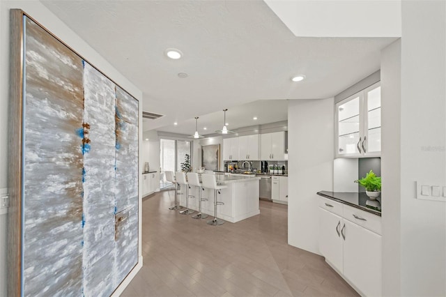 kitchen with white cabinets, dishwasher, a kitchen island, decorative light fixtures, and a kitchen bar