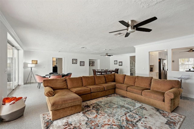 living area with visible vents, a ceiling fan, ornamental molding, stairs, and a textured ceiling