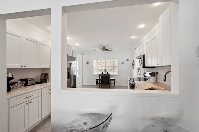 kitchen featuring stainless steel appliances, light countertops, ornamental molding, white cabinetry, and a sink