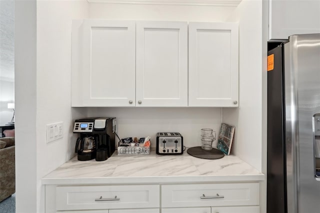 kitchen with stainless steel fridge, light stone counters, and white cabinets