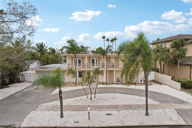 view of front of house with a balcony, driveway, fence, and stucco siding