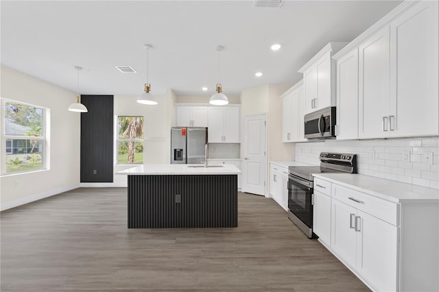 kitchen featuring light countertops, appliances with stainless steel finishes, a kitchen island with sink, and pendant lighting