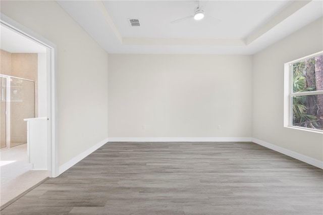 unfurnished room featuring light wood-style floors, a raised ceiling, ceiling fan, and baseboards