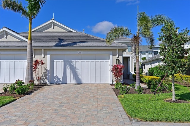 single story home featuring a garage, a tiled roof, decorative driveway, and stucco siding