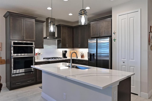 kitchen with a sink, appliances with stainless steel finishes, light stone countertops, wall chimney exhaust hood, and decorative light fixtures