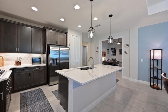 kitchen featuring stainless steel fridge, decorative light fixtures, light stone countertops, a kitchen island with sink, and a sink