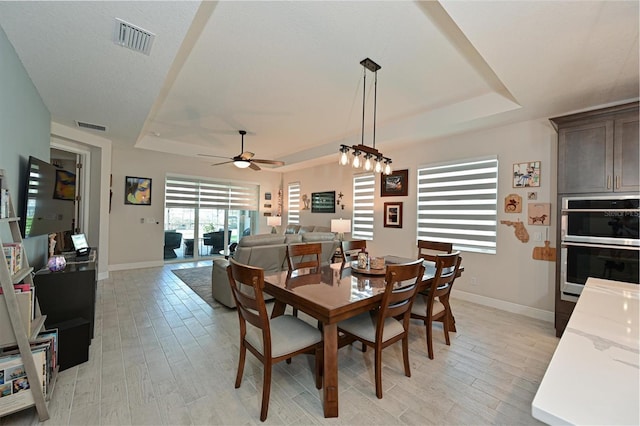 dining area with light wood finished floors, visible vents, and a tray ceiling