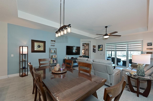 dining room featuring a raised ceiling, light wood-style flooring, ceiling fan, a textured ceiling, and baseboards