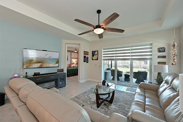 living area featuring baseboards, a raised ceiling, and a ceiling fan