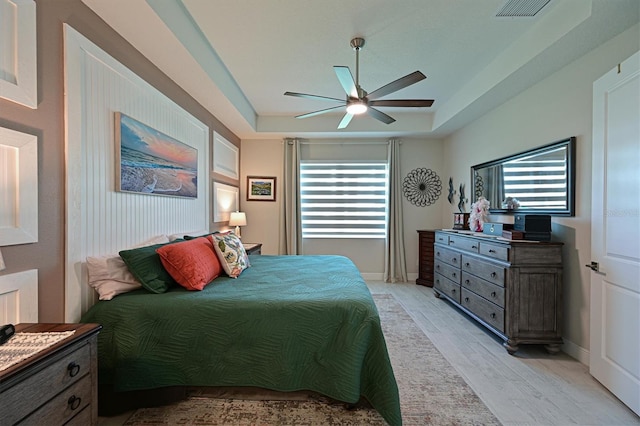 bedroom featuring ceiling fan, visible vents, baseboards, light wood finished floors, and a raised ceiling