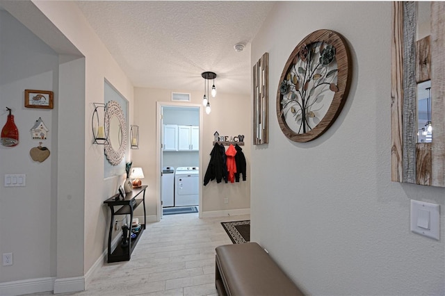 hallway featuring a textured ceiling, visible vents, baseboards, light wood-type flooring, and washing machine and clothes dryer