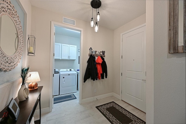 doorway to outside with a textured ceiling, visible vents, baseboards, light wood finished floors, and washing machine and clothes dryer