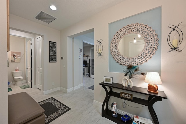 hall featuring light wood finished floors, baseboards, and visible vents