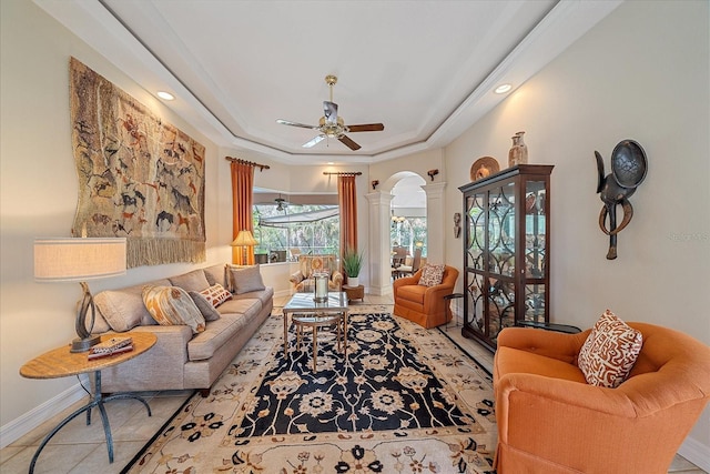 tiled living area with arched walkways, decorative columns, a raised ceiling, ceiling fan, and baseboards