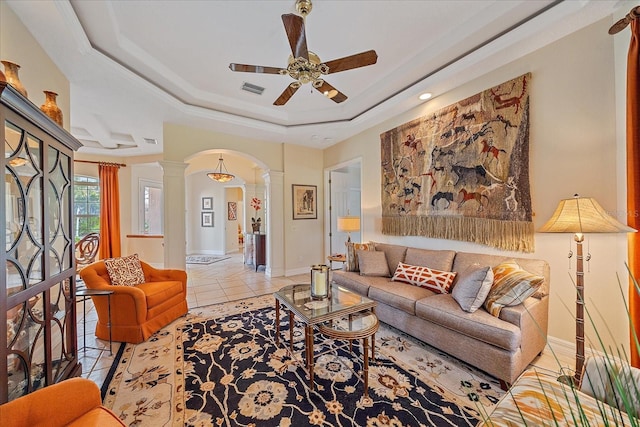 living area with light tile patterned floors, decorative columns, arched walkways, a raised ceiling, and a ceiling fan