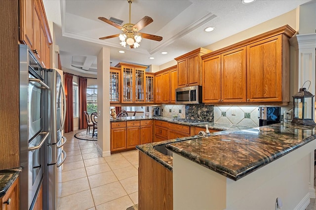 kitchen featuring a peninsula, a tray ceiling, glass insert cabinets, and appliances with stainless steel finishes