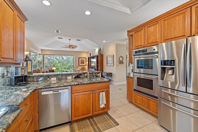 kitchen featuring stainless steel appliances, dark stone counters, brown cabinetry, and a tray ceiling