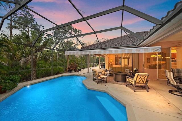 pool at dusk featuring glass enclosure, a patio area, an outdoor living space with a fire pit, and an outdoor pool