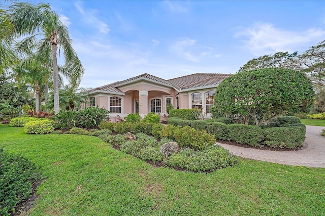 mediterranean / spanish-style home featuring a tiled roof, a front lawn, and stucco siding