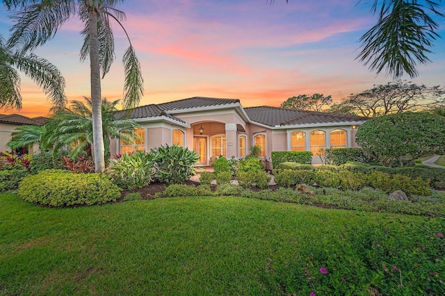 view of front of property featuring a tile roof, a lawn, and stucco siding