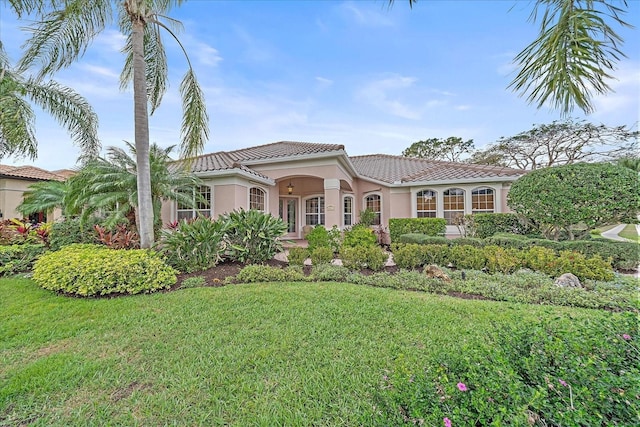 mediterranean / spanish home with a front yard, a tile roof, and stucco siding