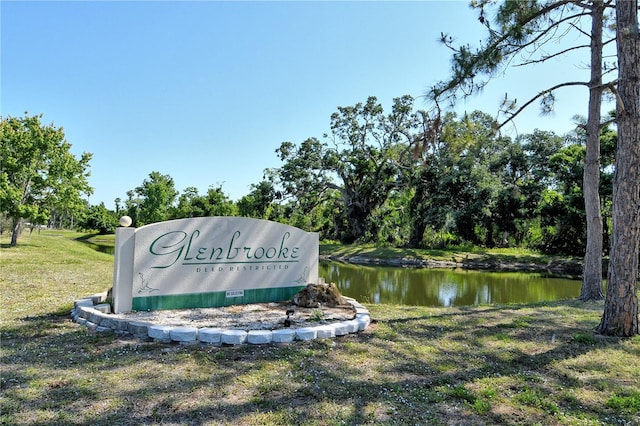 community / neighborhood sign featuring a lawn and a water view