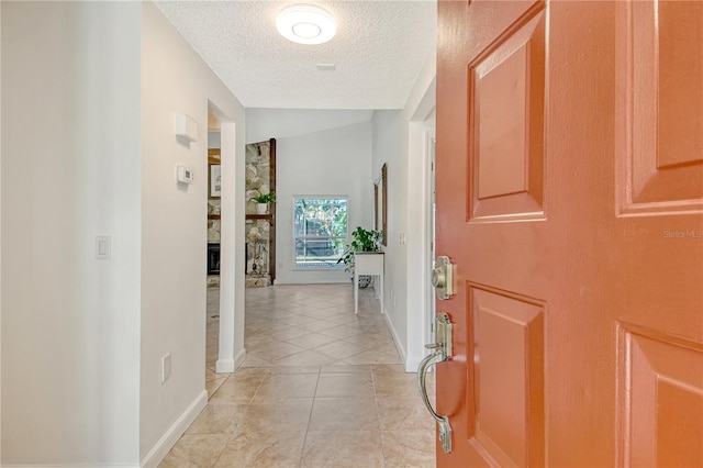 hallway with a textured ceiling, baseboards, and light tile patterned floors