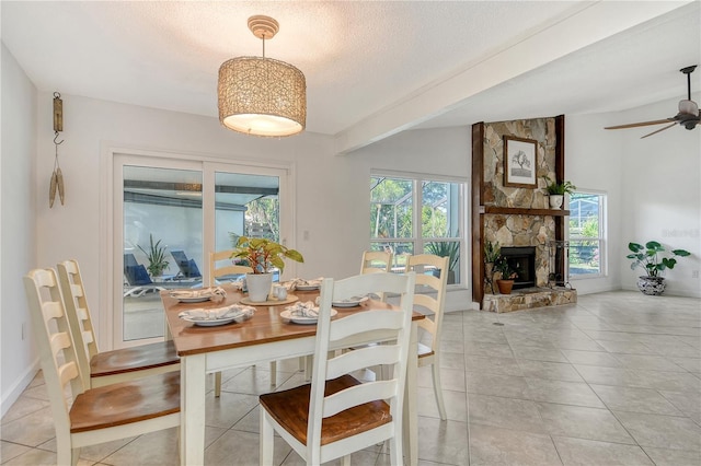 dining area with ceiling fan, a textured ceiling, a fireplace, light tile patterned floors, and baseboards