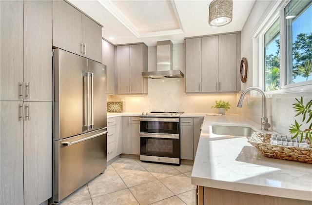 kitchen featuring gray cabinets, wall chimney exhaust hood, a raised ceiling, a sink, and appliances with stainless steel finishes