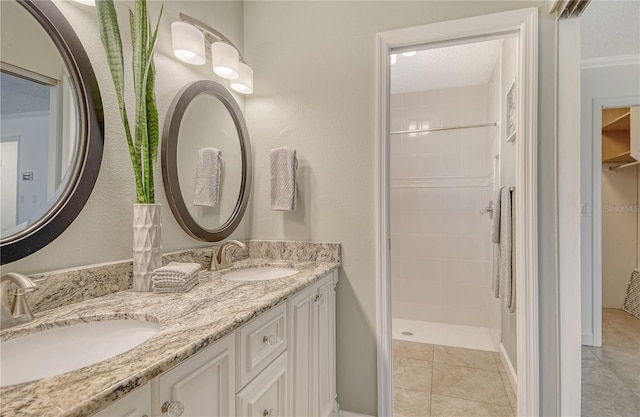 bathroom featuring double vanity, tile patterned floors, tiled shower, and a sink