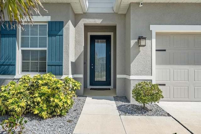 entrance to property featuring an attached garage and stucco siding