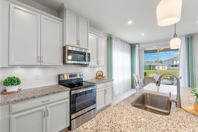 kitchen with light stone counters, a sink, appliances with stainless steel finishes, tasteful backsplash, and decorative light fixtures