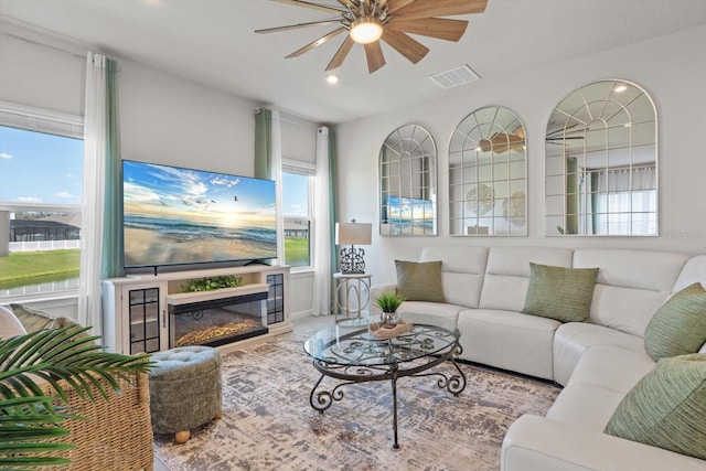 living room with a glass covered fireplace, visible vents, and a ceiling fan